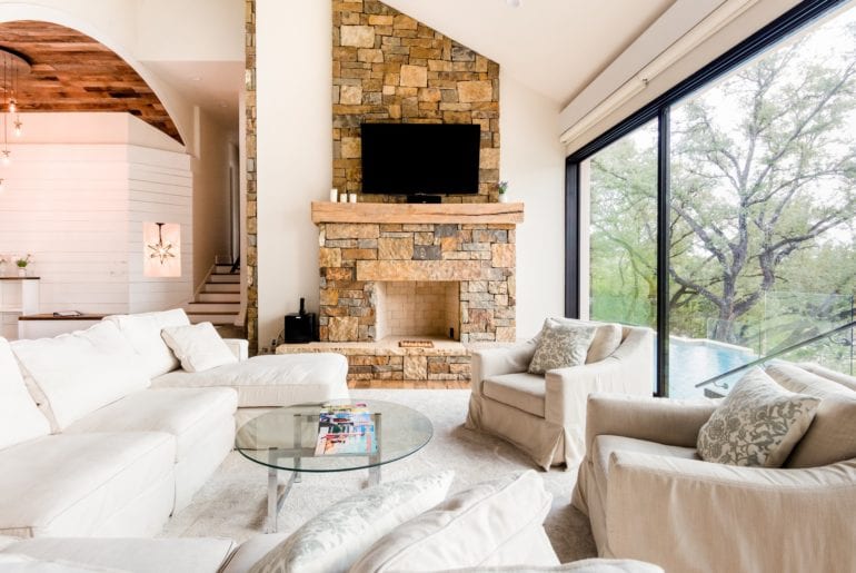 The living room has a stone fireplace, with enormous sliding glass doors and cozy white sofas.