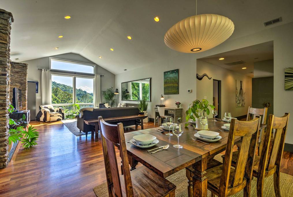 Open floor plan living and dining room, featuring rugged dining table, stacked stone wall, and cow skin arm chair