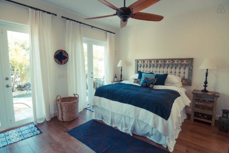 a bed with blue blanket on it and a fan above it