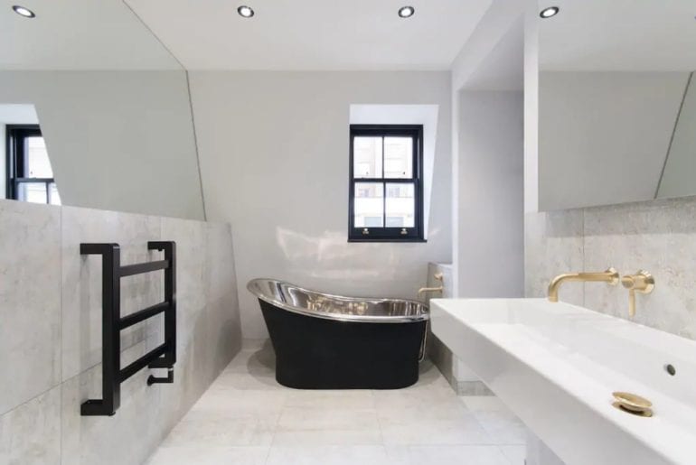 a stand alone silver bathtub in an angular bathroom