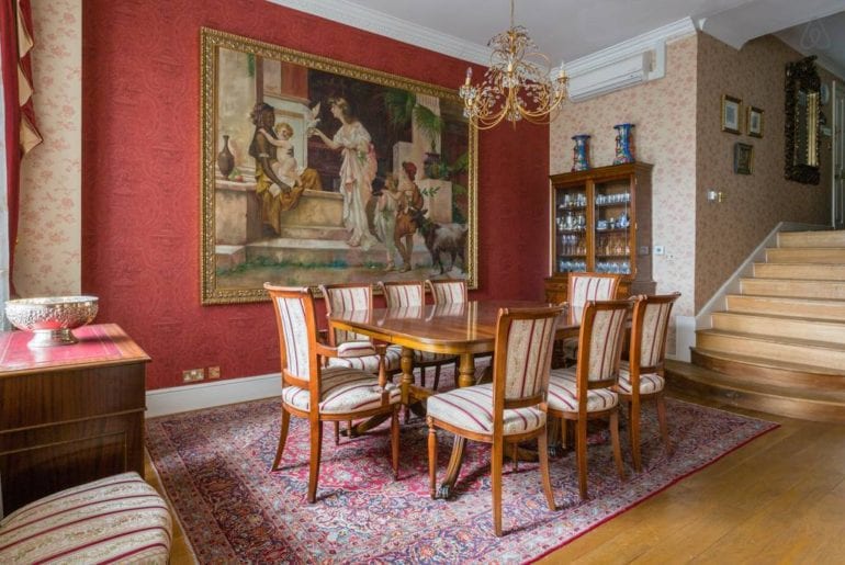 A wooden dining table with a painting behind it and a chandelier over it